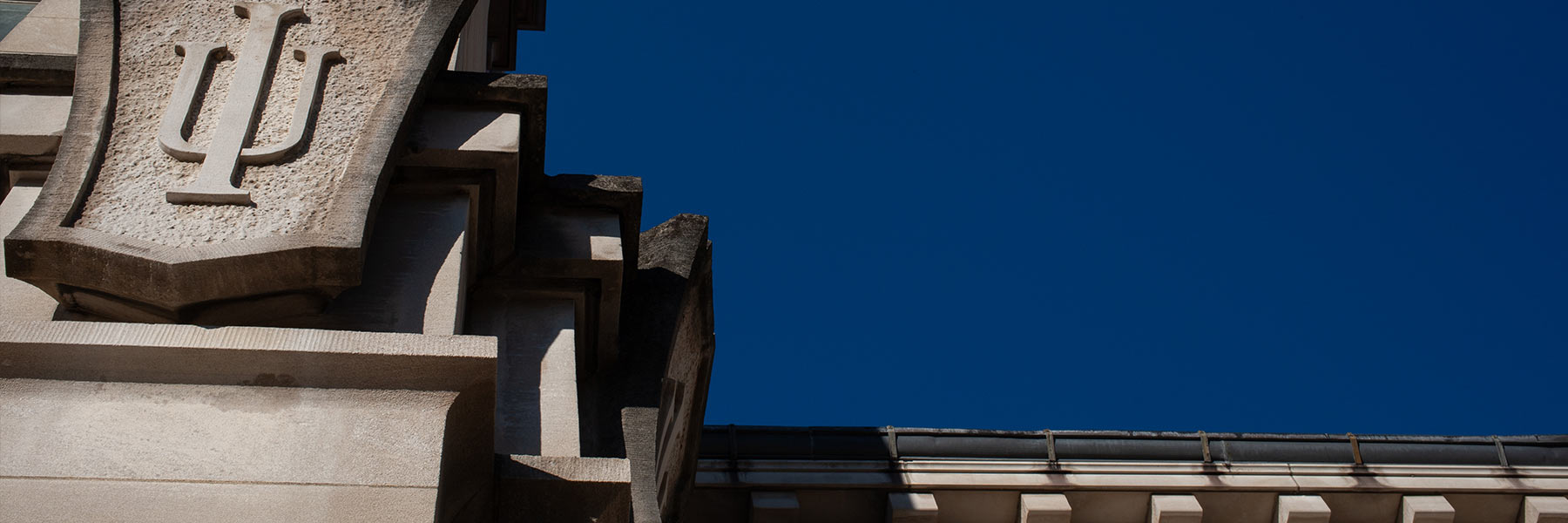 Campus building detail featuring the IU trident against a blue sky