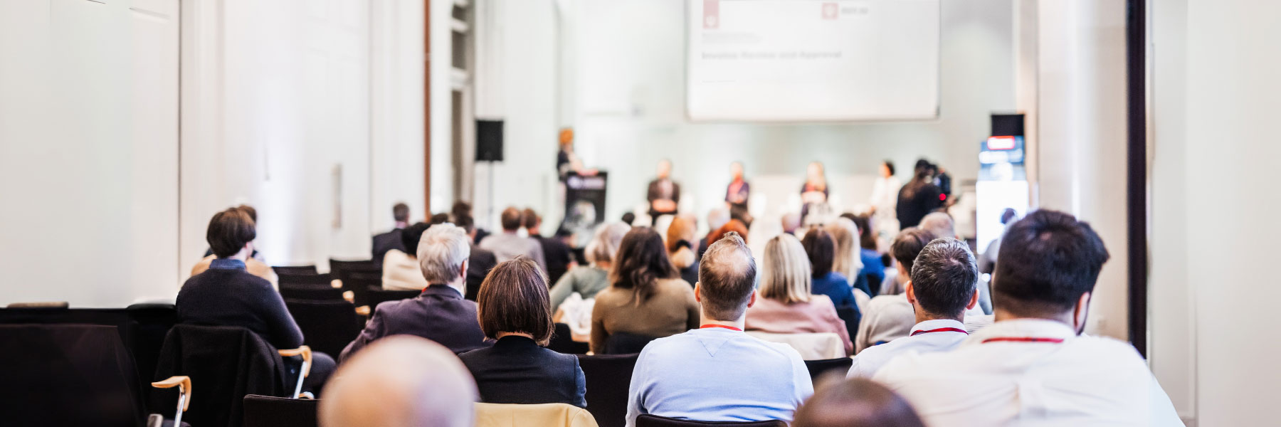 Conference session showing the backs of people's heads and people on a stage